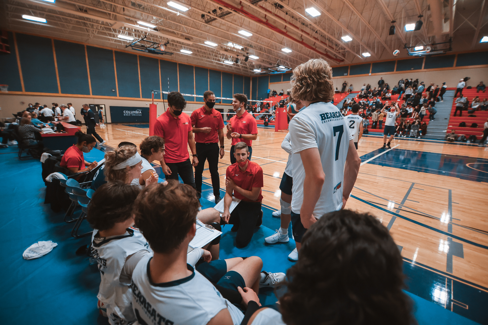 Bearcats men's volleyball team and coach discussing on the bench.