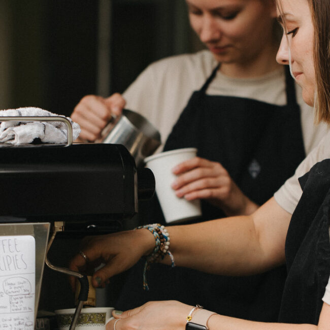 two women make coffee at an espresso machine