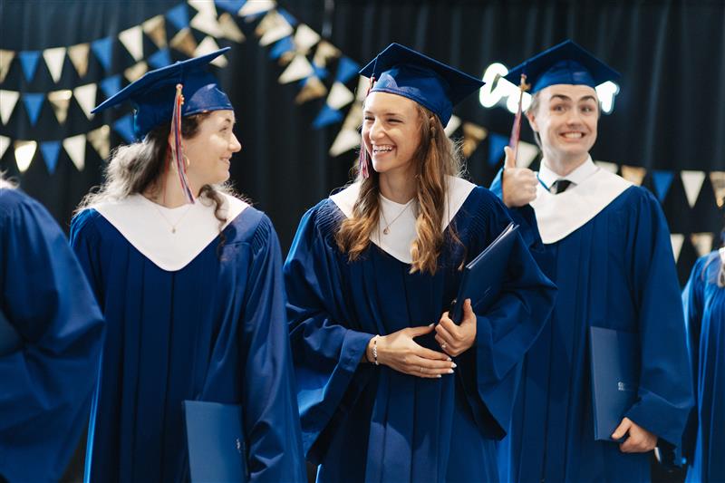 Three Columbia Bible College graduates in caps and gowns